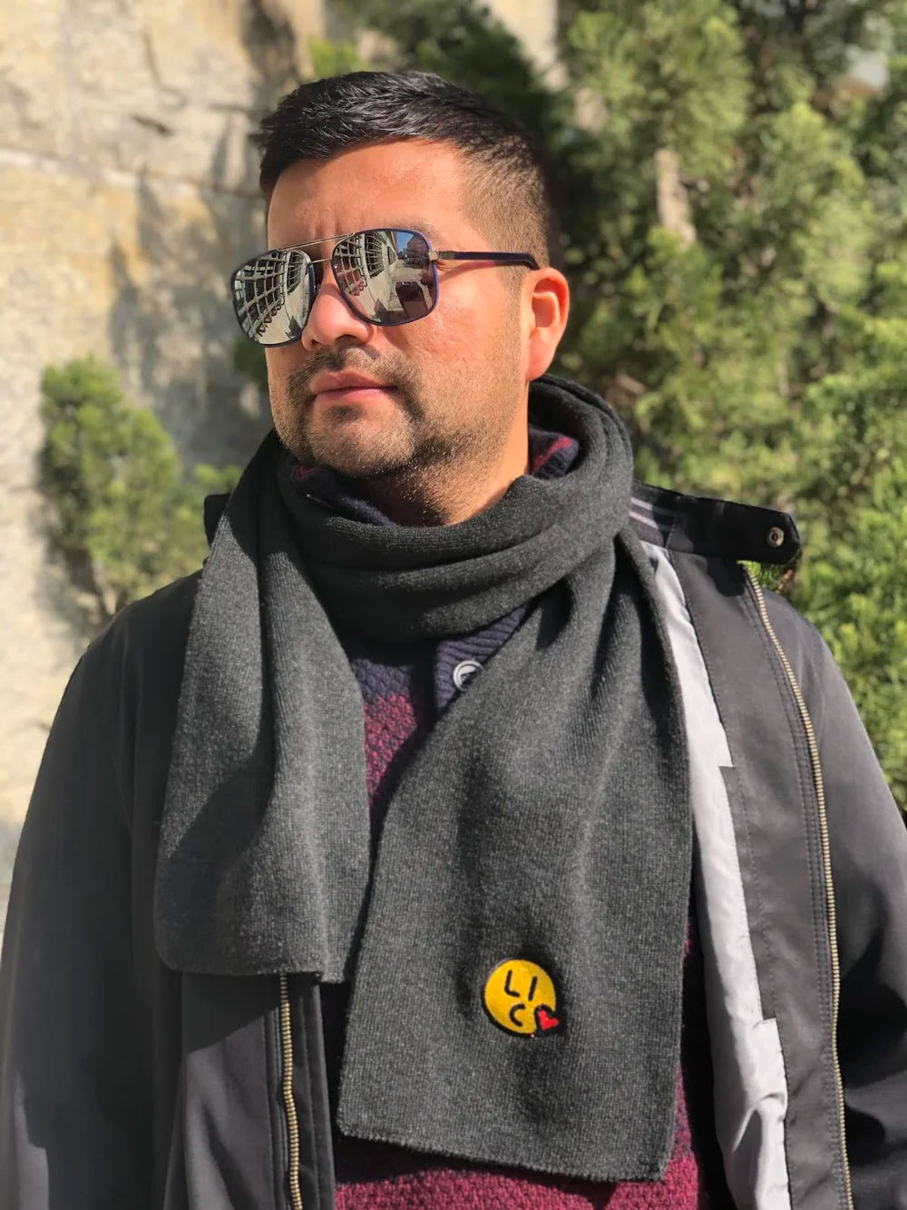 Man wearing sunglasses and a dark scarf with a yellow "Long Island City" logo, standing outdoors.