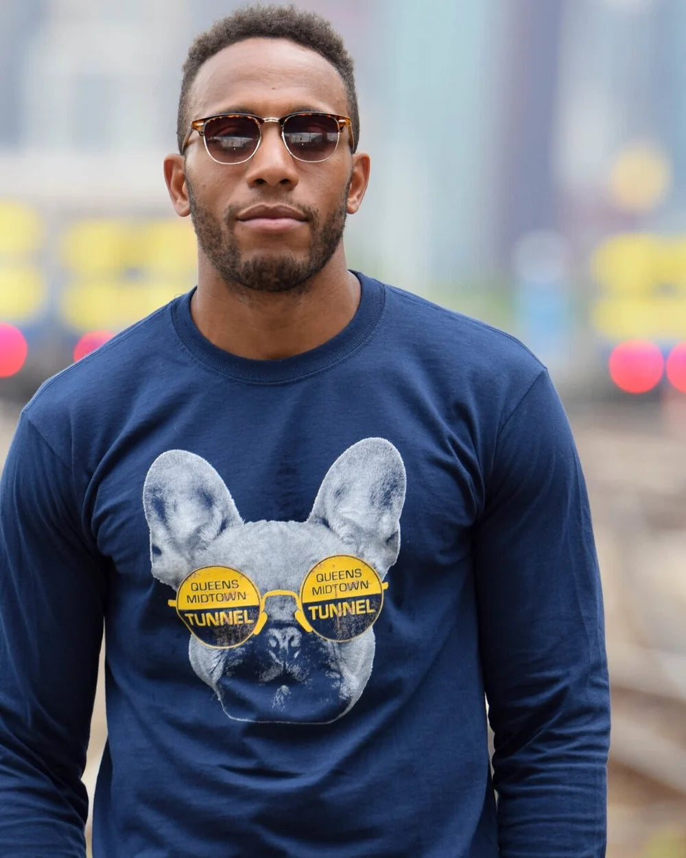 Man wearing a navy blue long-sleeve shirt with a graphic of a dog and sunglasses, standing in an urban setting.