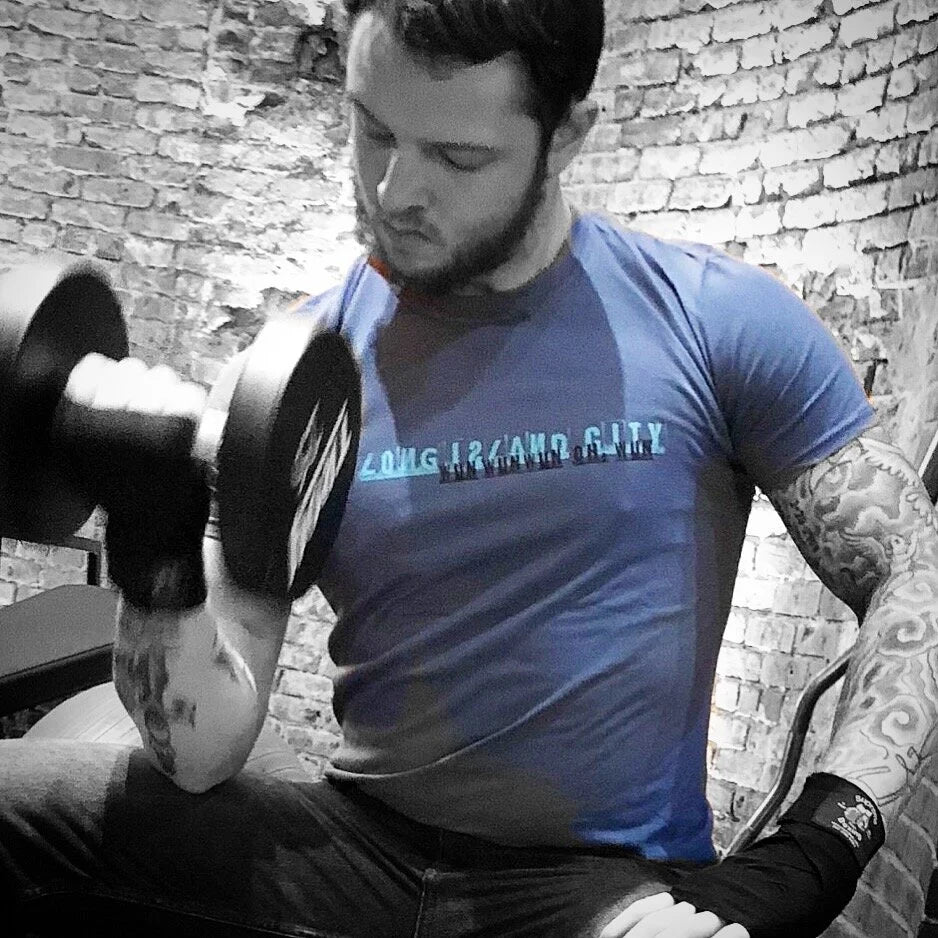 Man lifting weights wearing a blue t-shirt with Long Island City graphic text on a blurred background