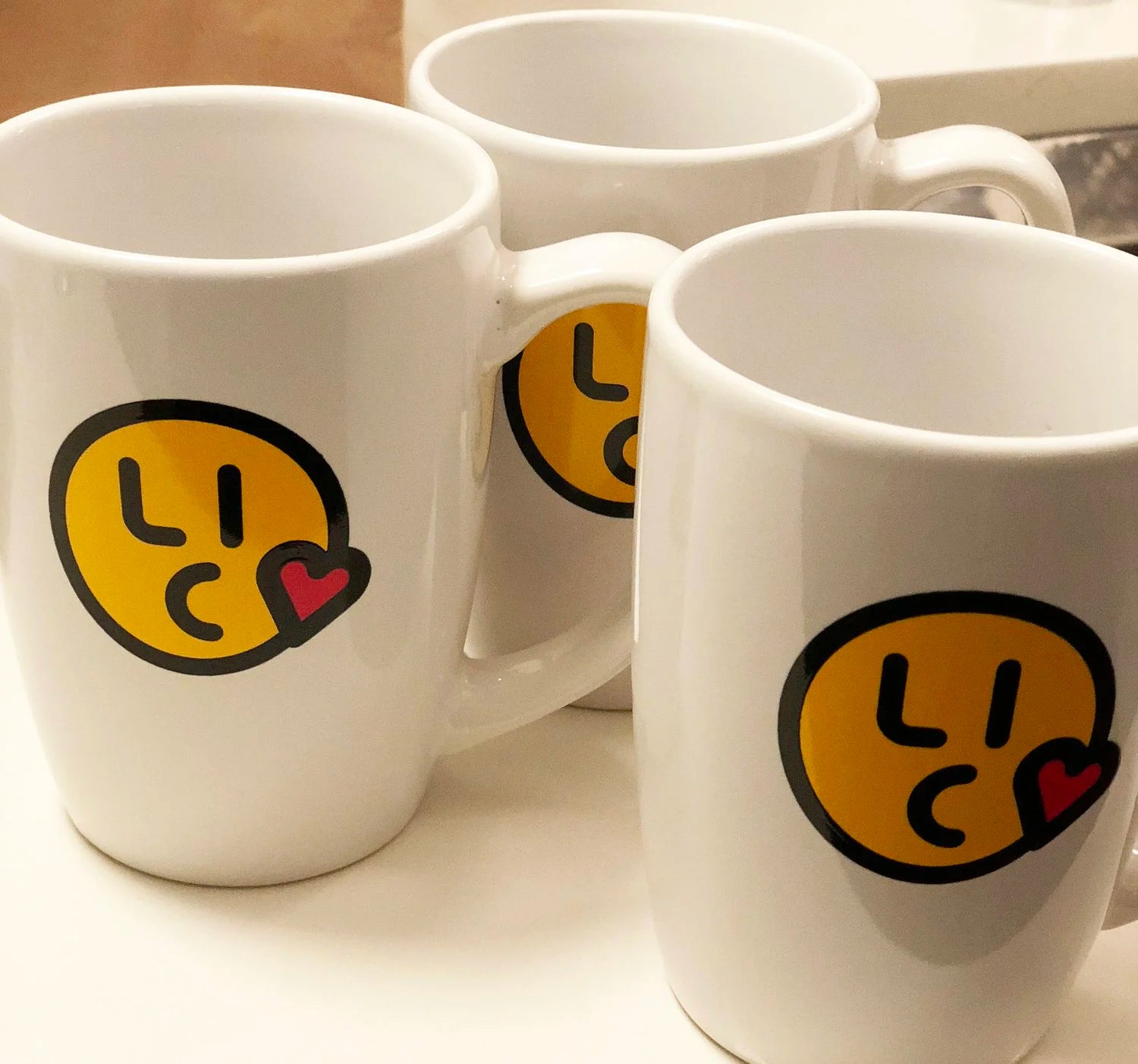 Three white mugs with smiley face designs and 'LIC' text on a light background