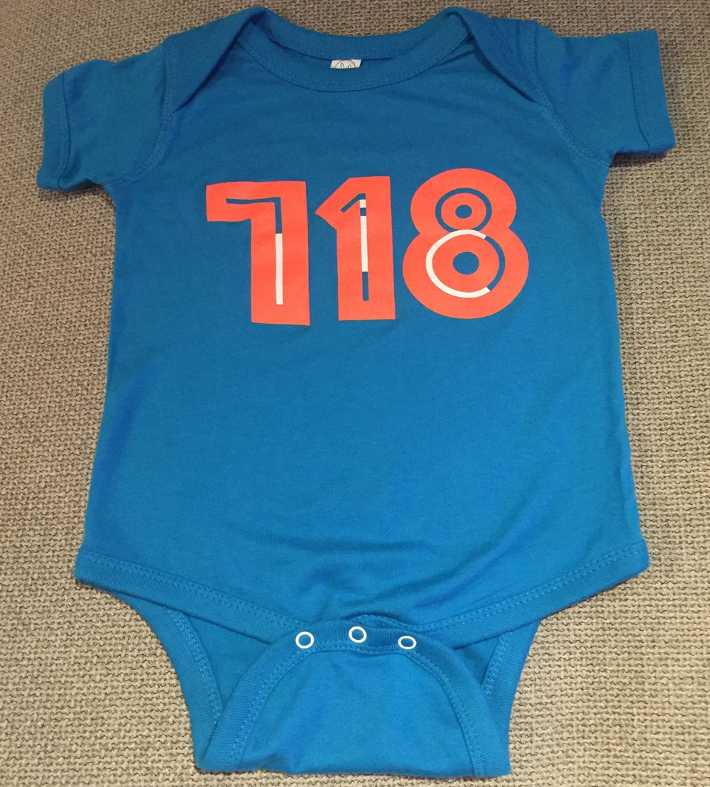 Blue baby onesie with red '718' print on a beige carpet