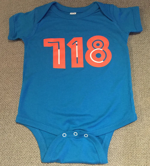 Blue baby onesie with red '718' print on a beige carpet
