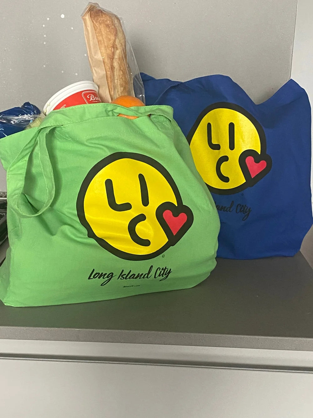 Green and blue tote bags with smiley face 'Long Island City' logo