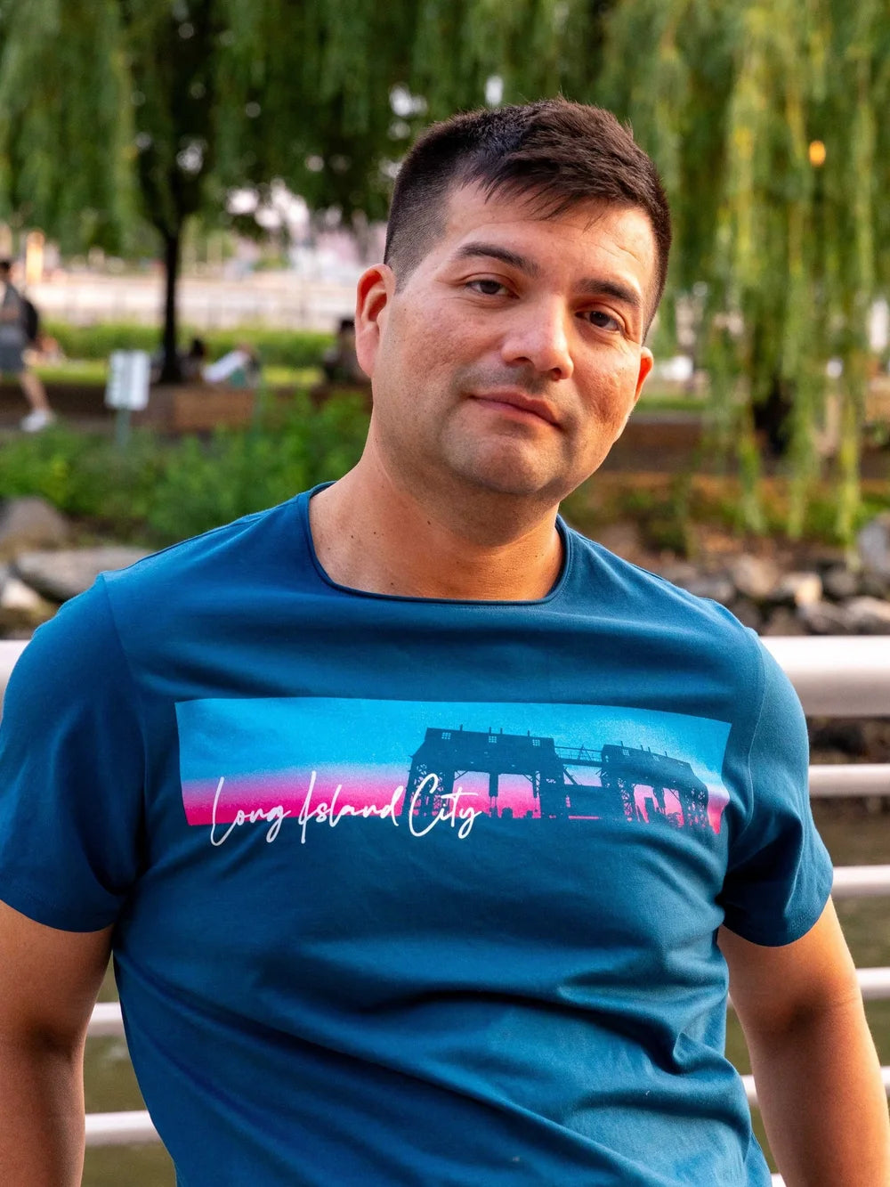 Man wearing a blue t-shirt with Long Island City text and a colorful graphic design outdoors.