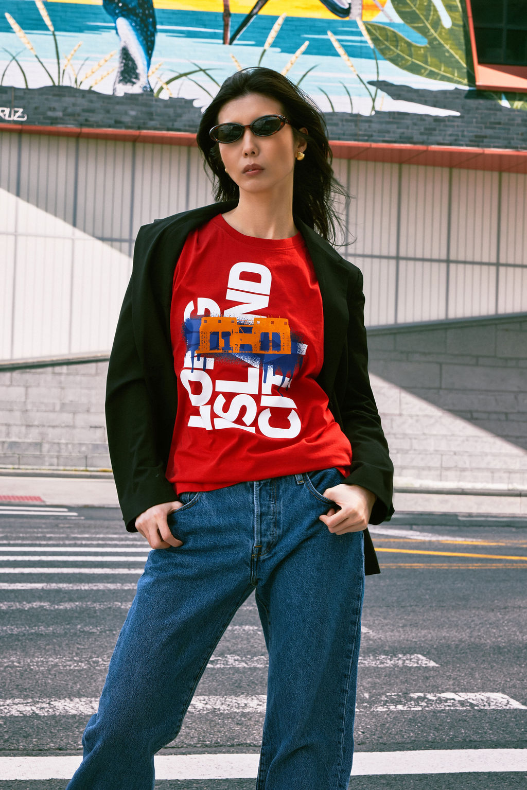 Person wearing a red graphic t-shirt with blue jeans standing on a street.