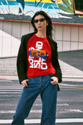 Person wearing a red graphic t-shirt with blue jeans standing on a street.