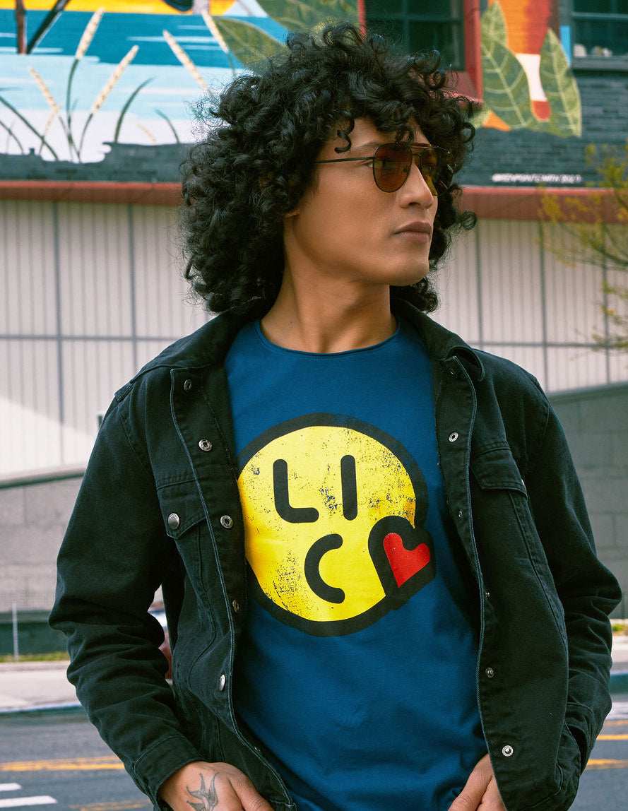 Person wearing a blue t-shirt with a yellow logo and black jacket outdoors.