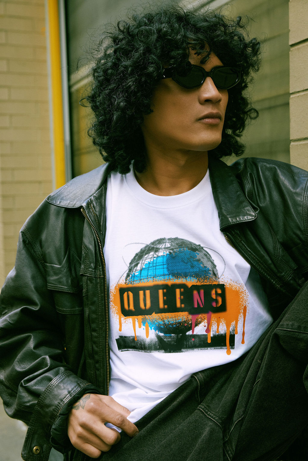 Person wearing a white t-shirt with 'QUEENS' graphic design, standing outdoors.