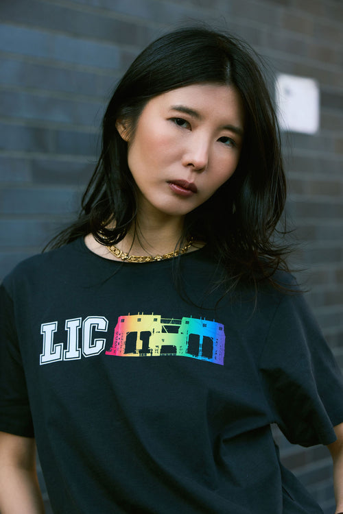 Person wearing a black t-shirt with colorful 'LIC' graphic against a brick wall.