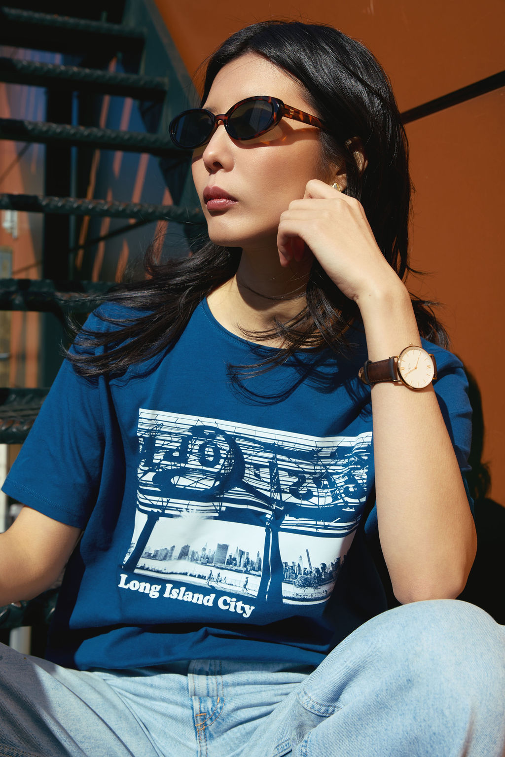 Woman wearing a blue t-shirt with a graphic design, sitting outdoors.