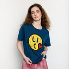 Woman wearing a blue t-shirt with a yellow smiley face design on a plain background