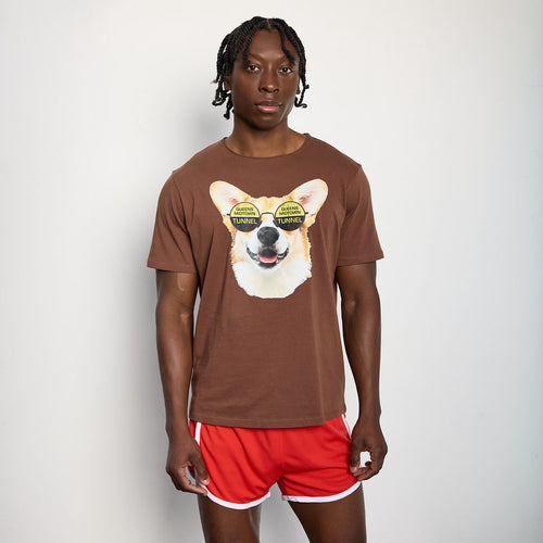 Person wearing a brown t-shirt with a dog graphic and red shorts on a plain background