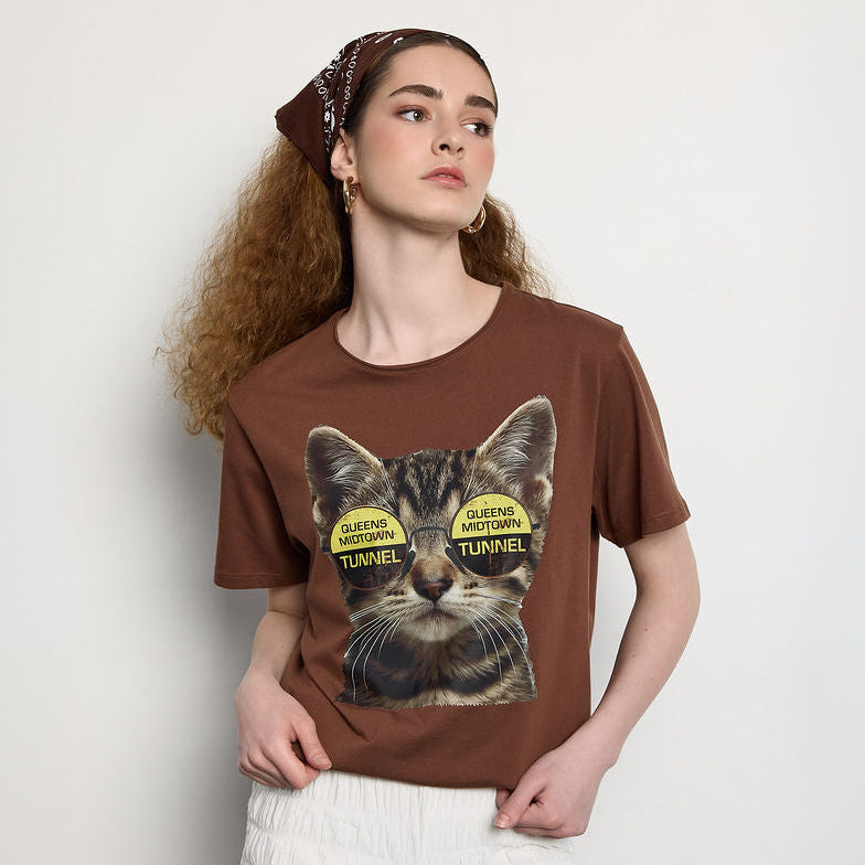 Woman wearing a brown t-shirt with a cat graphic and text on a plain background