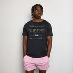 Person wearing a black t-shirt with text and graphics, paired with pink shorts on a plain background