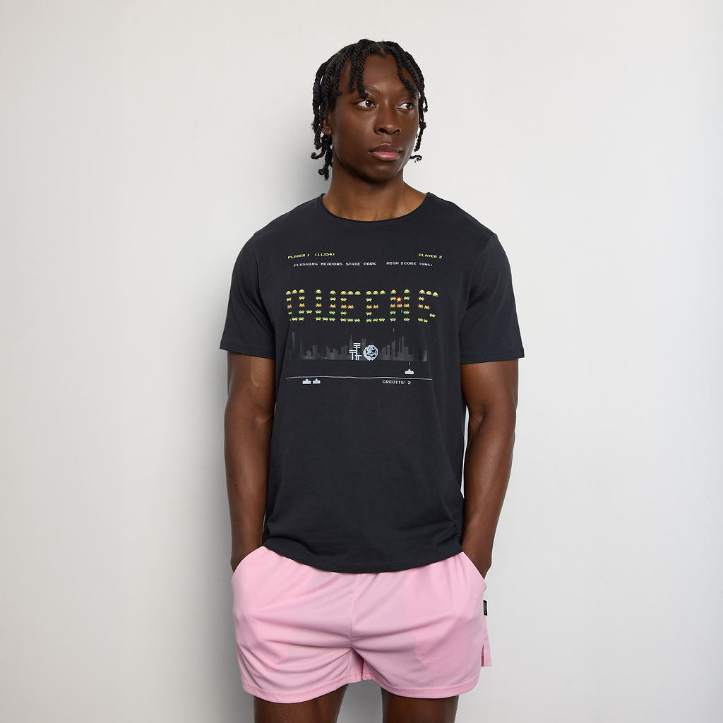 Person wearing a black t-shirt with text and graphics, paired with pink shorts on a plain background