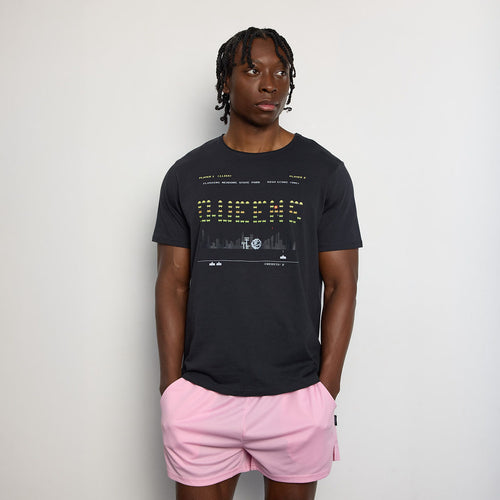 Person wearing a black t-shirt with text and graphics, paired with pink shorts on a plain background