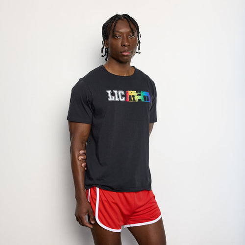 Person wearing a black t-shirt with colorful text and red shorts on a light gray background