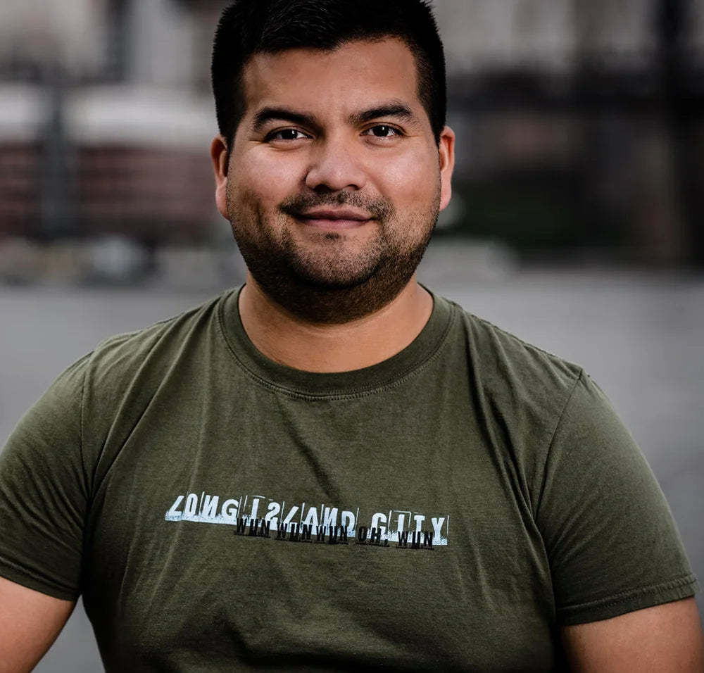 Man wearing a dark green t-shirt with Long Island City graphic text on a blurred background
